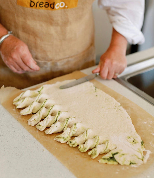 Gluten Free savoury dough shaped into tree. One side is cut into strips and twisted. The baker is holding a knife and cutting strips on the other side. 