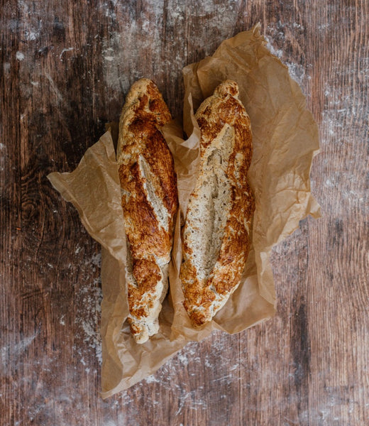 Two Gluten Free Rustic White baguettes on baking paper on a dark brown wooden bench 