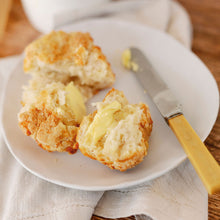 Load image into Gallery viewer, Buttered scone on a plate with a knife, on a wooden table.