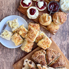 Load image into Gallery viewer, Assorted scones with jam and clotted cream on a wooden table.