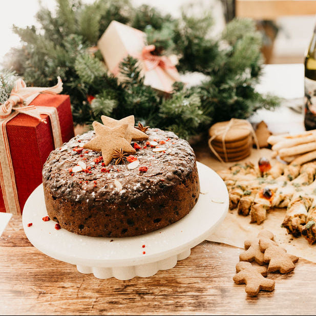 Christmas-themed table setting with a fruit cake, cookies, and a bottle of wine.