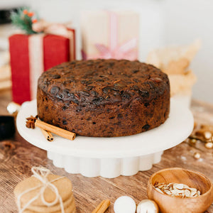 Christmas fruit cake on a white stand with festive decorations in the background