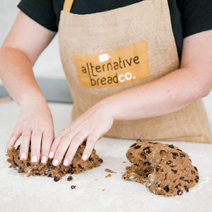 Lady wearing hessian Alternative Bread Company apron  dividing gluten free hot cross bun dough in half 