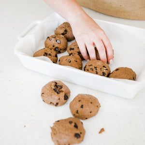 Placing gluten free hot cross buns into a white baking dish lined with baking paper. 