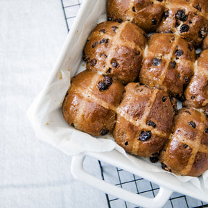 Gluten free hot cross buns  in a white baking dish. taken on a angle with a black rack and white table cloth 
